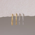 The Bold Pave Oval Hoops set features two pairs of thin, textured statement earrings in gold and silver, displayed on a torn paper background—ideal for adding a touch of sparkle to any outfit.