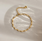 Eternity Pearl Bracelet: This elegant piece showcases pearls on a gold infinity chain, beautifully displayed flat on a beige surface with gentle, soft light reflections.
