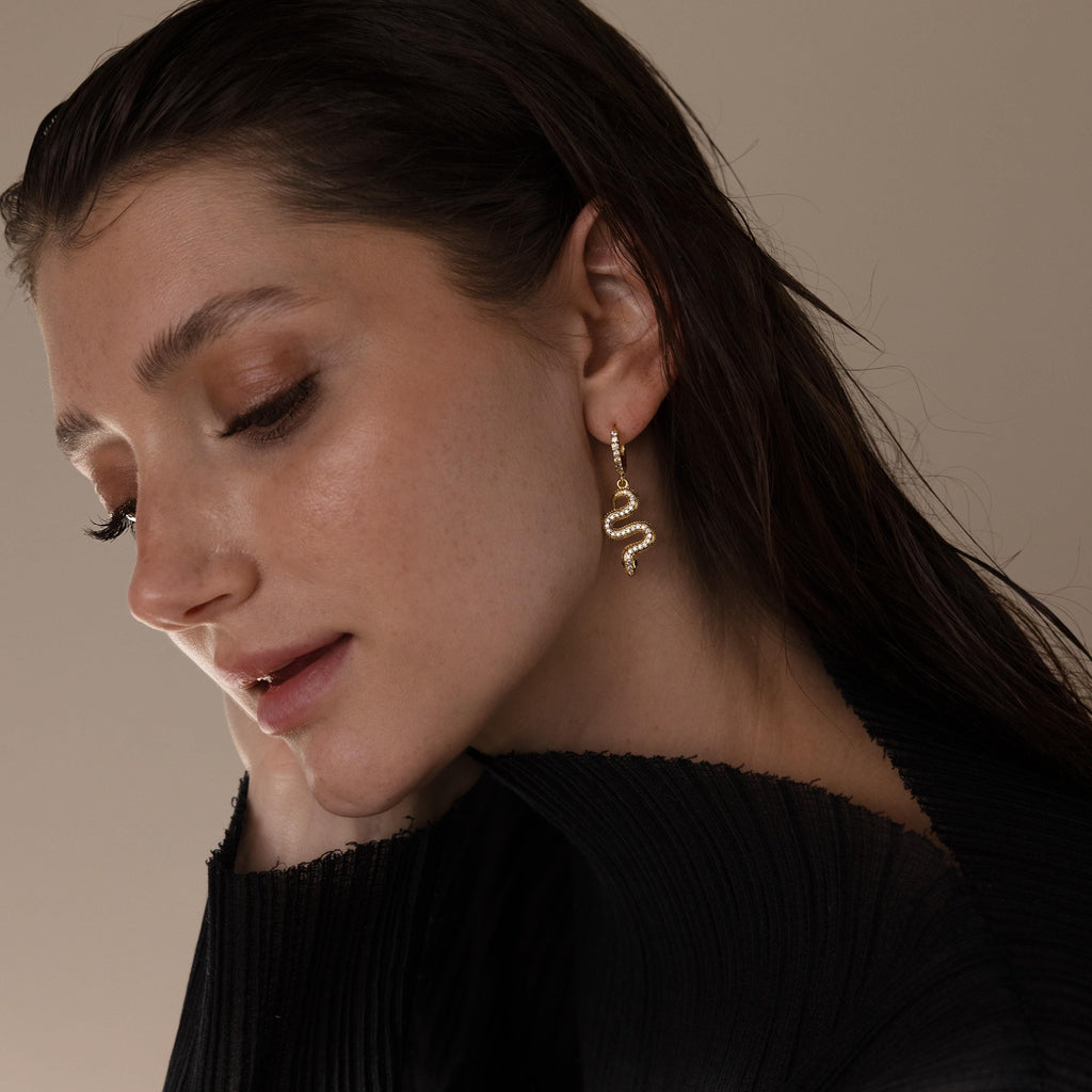 Woman with wet hair wearing the gold Pave Snake Charm Hoops and a black top, looking down gently.