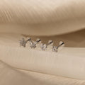 The Pave Assortment Flat Back Set features four earrings, each with a distinct crystal shape, displayed on cream fabric. This elegant set brings sparkle and style to any look.