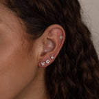 Close-up of a woman's ear wearing the Pave Assortment Flat Back Set, featuring pave diamond studs and flower-shaped earrings on her lobe and cartilage.