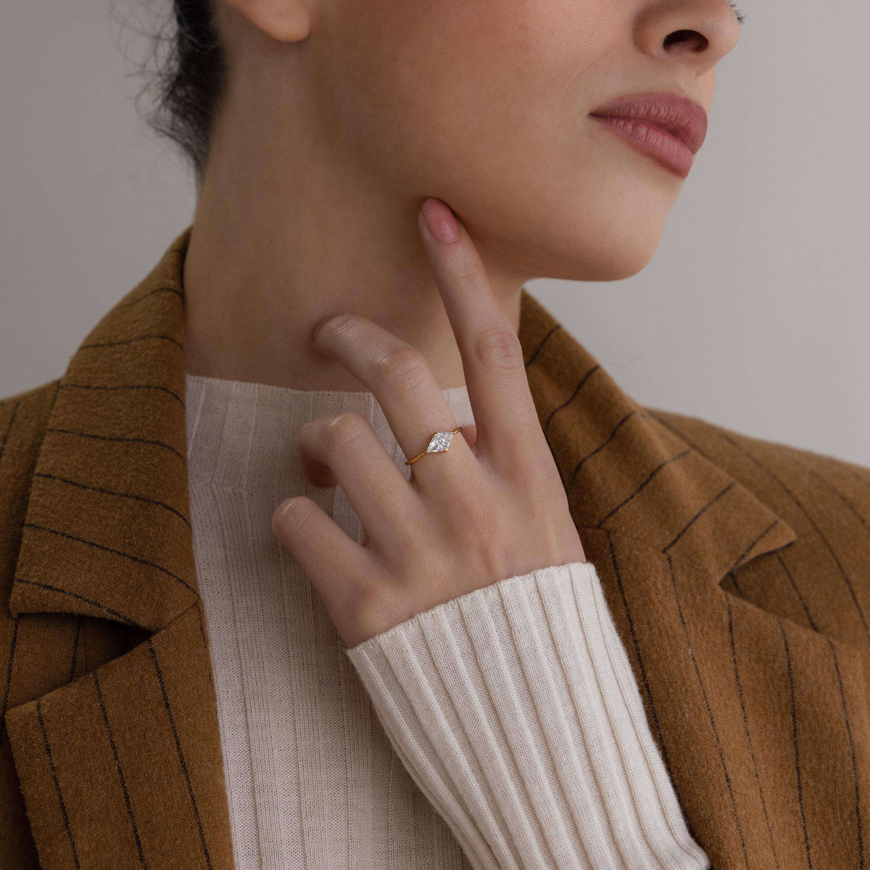 A woman wearing the Toi et Moi Triangle Birthstone Ring touches her chin, styled in a brown blazer and cream sweater.