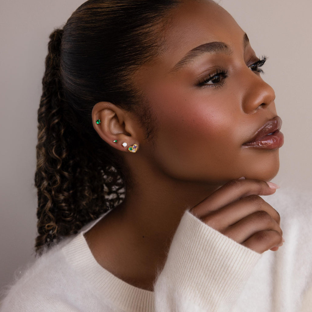 A woman with her hand on her chin, displaying Mixed Birthstone Heart Studs—elegant earrings featuring customizable gemstones.