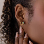 Close-up of a person wearing Mixed Birthstone Heart Studs—gold heart-shaped earrings featuring customizable red, blue, and green gemstones.