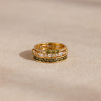 Close-up of three stacked gold peridot and diamond rings placed on a neutral fabric surface.