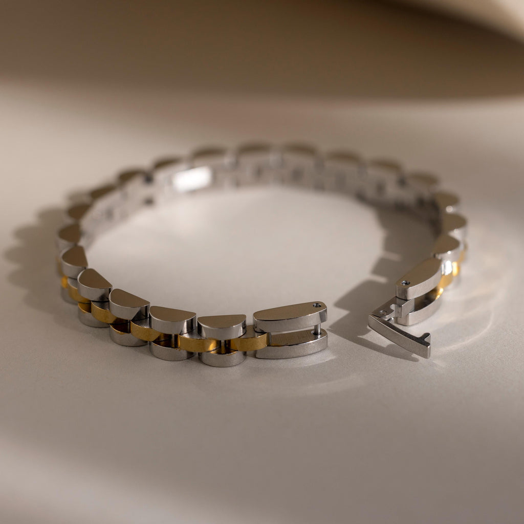 The Mixed Metal Link Bracelet in silver and gold, featuring a secure clasp, is elegantly displayed on a neutral surface in soft lighting—making it the perfect gift for him.