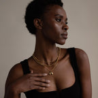 Woman in a black top wears layered gold necklaces, including the Bubble Letter Necklace, as she looks to the side with a neutral expression.