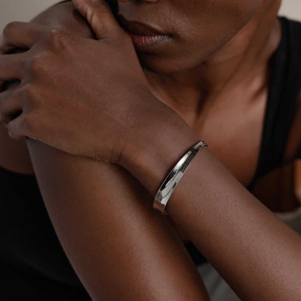A close-up shows a person wearing the Dome Cuff Bracelet on their wrist with arms crossed—this elegant cuff adds a chic touch to any outfit.