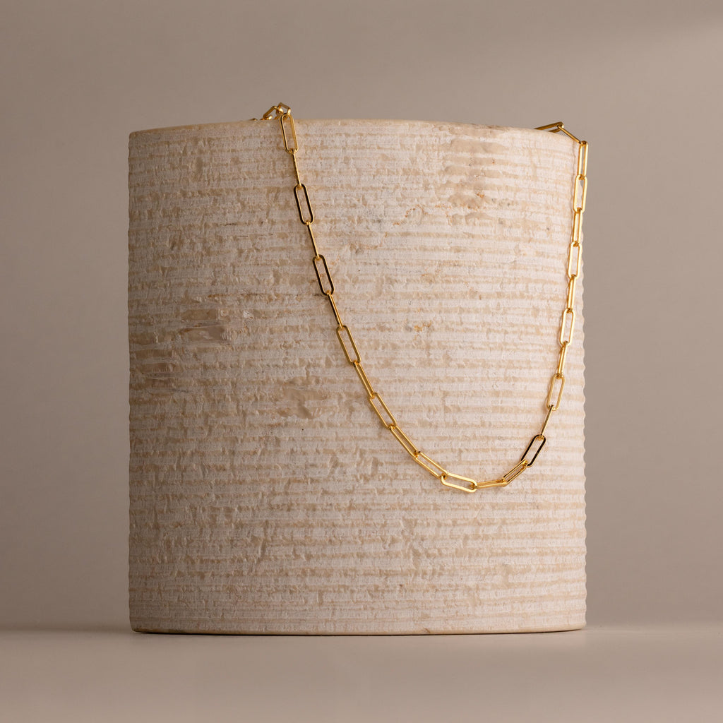 The Bold Paperclip Chain Necklace features rectangular links draped over a textured, cylindrical beige stone—a striking statement piece for any look.