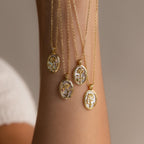 The Pearl Flower Birthstone Necklace, featuring a unique floral design in an oval frame with pearl accents, hangs from a raised arm against a neutral background.
