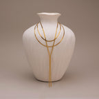 The Long Y Herringbone Chain Necklace is displayed draped over a white textured vase, set against a neutral background.