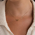 Wearing the Pave Interlocking Circle Necklace, featuring two linked gold rings symbolizing love, over a cream textured shirt.