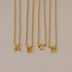 Four Dainty Bubble Letter Necklaces in 18K Gold, featuring A, B, C, and D pendants, displayed on a neutral background—ideal for a minimalist personalized accessory.