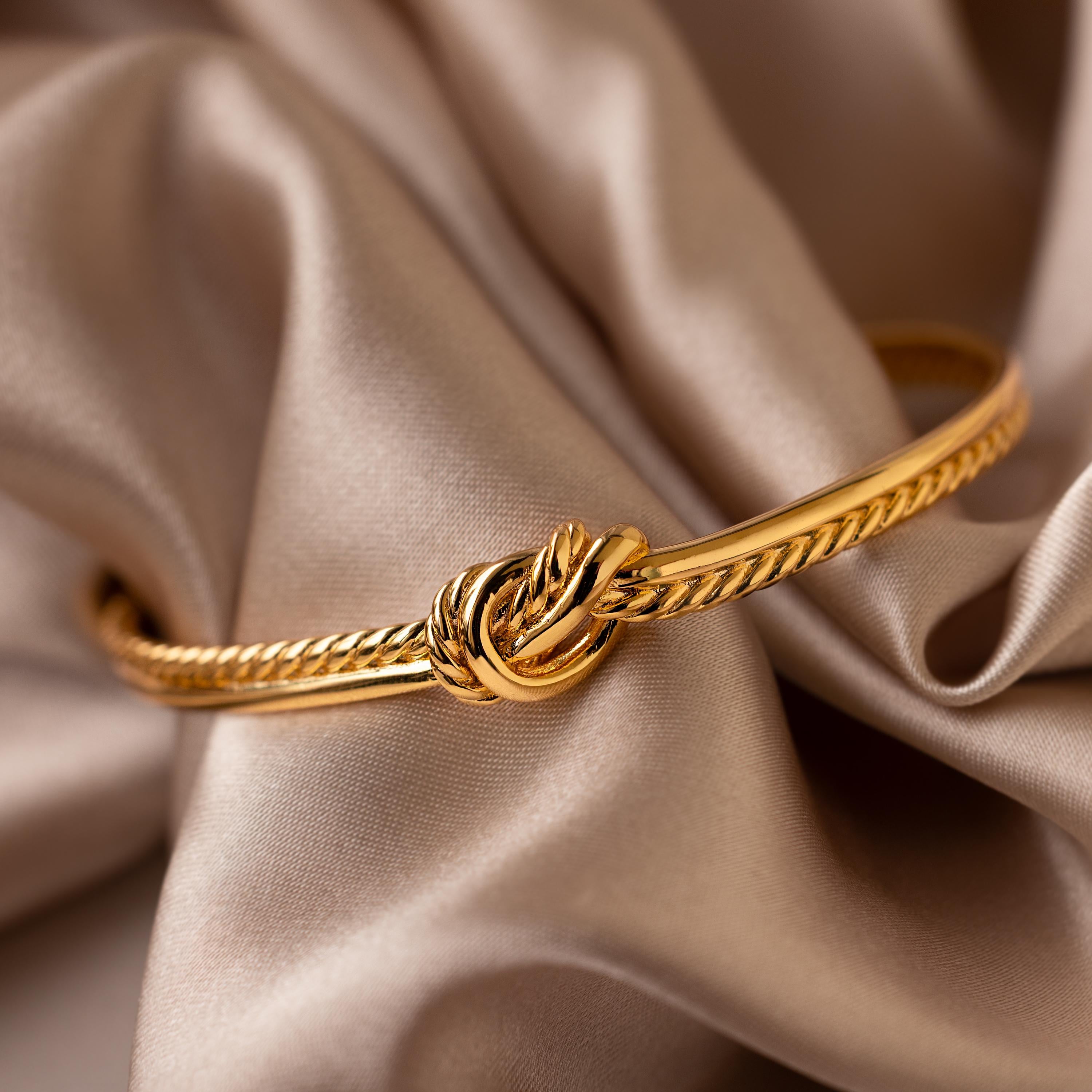 The Duo Knot Bangle, featuring a unique rope texture in gold, is stylishly presented on beige silky fabric—making it the perfect elegant gift.