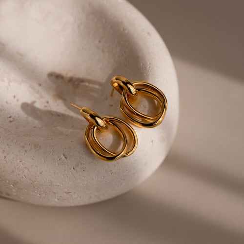 Bold Duo Knot Earrings shown on a smooth, pale stone surface with gentle natural light, emphasizing their sculptural elegance.