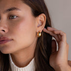 A woman in a white turtleneck shows off the Bold Disco Earrings, touching her ear for a hint of retro glam.