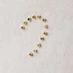 Square Bezel Pink Tourmaline Flatback Studs, along with other small colorful gemstones, are arranged in a question mark shape on a textured beige surface.