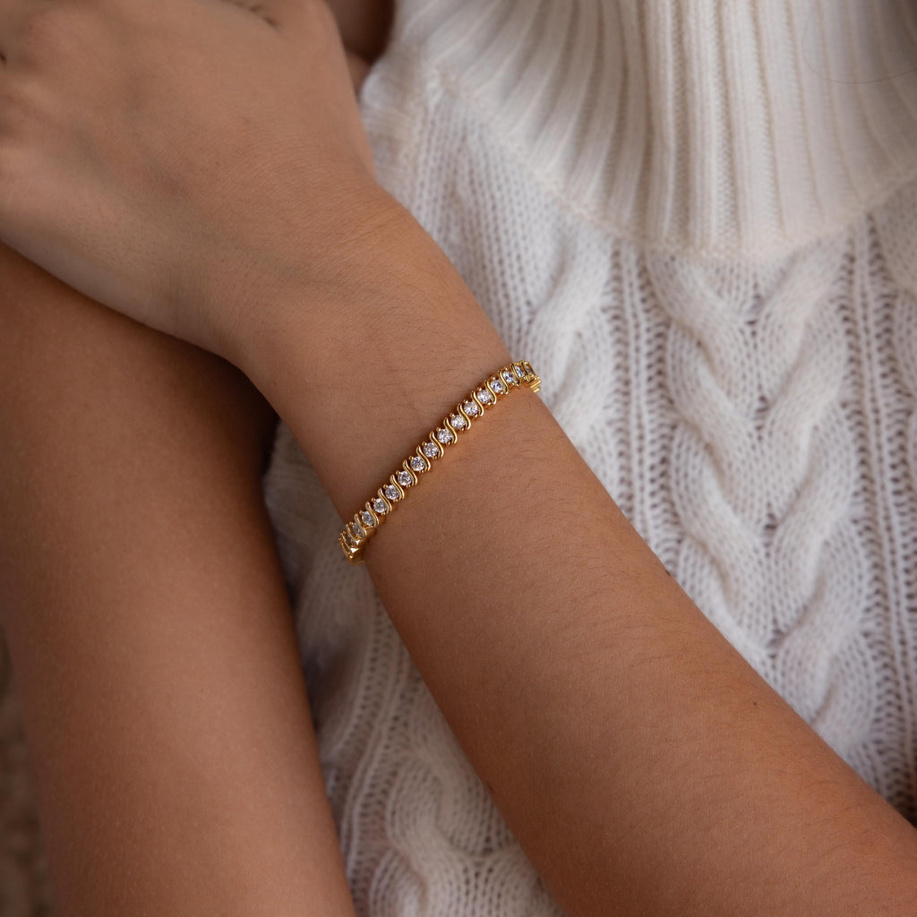 The S-Link Diamond Tennis Bracelet in 18K Gold graces a woman's wrist, paired with a white cable knit sweater for an effortlessly elegant jewelry look.