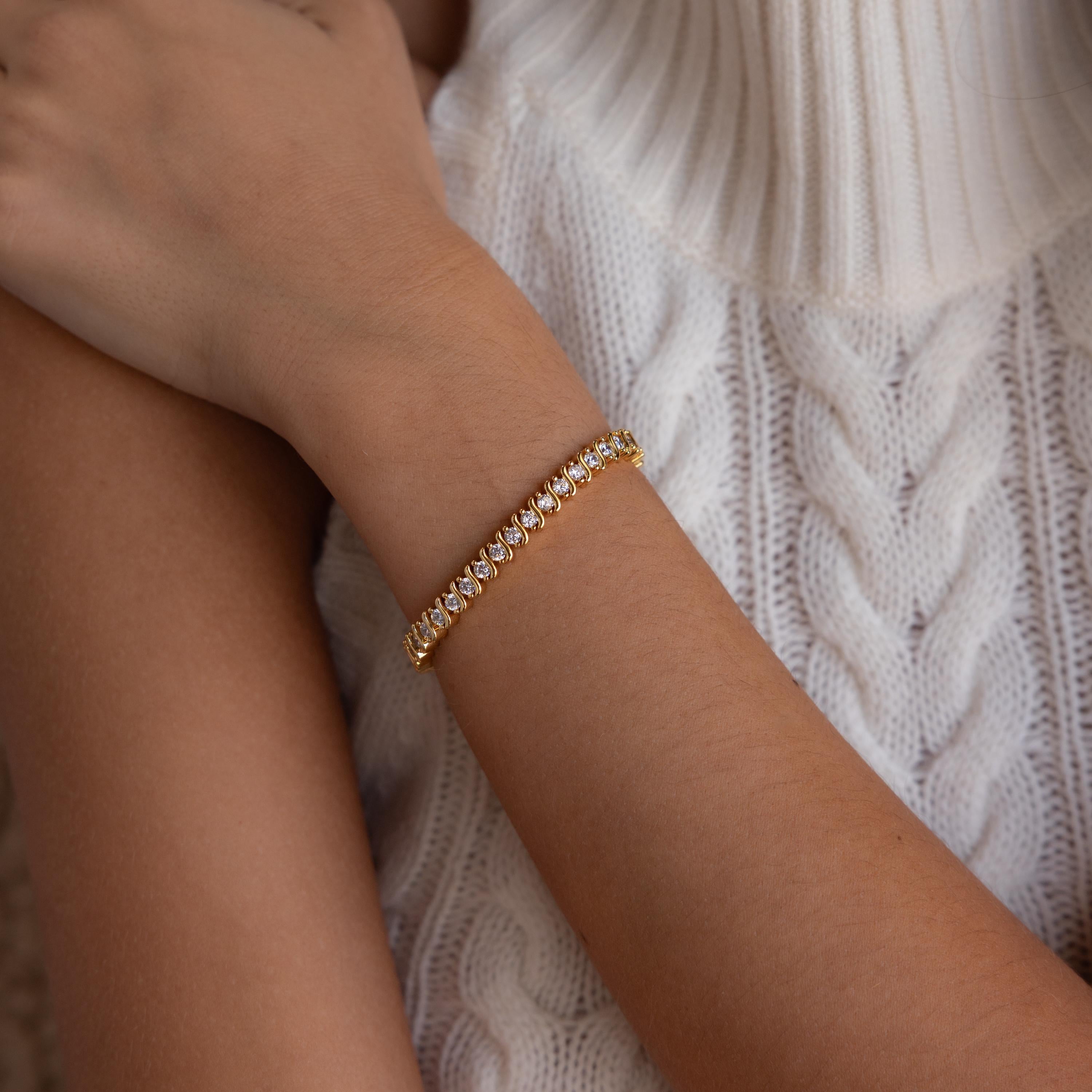 The S-Link Diamond Tennis Bracelet in 18K Gold graces a woman's wrist, paired with a white cable knit sweater for an effortlessly elegant jewelry look.