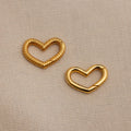 The Heart Carabiner Set in 18K Gold features two heart-shaped charms—one twisted, one smooth—perfect as a bracelet connector or jewelry set accent, displayed on beige textured fabric.