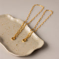 The Paperclip Clasp Necklace, a striking gold chain, is elegantly displayed on a speckled ceramic dish set against a beige background.