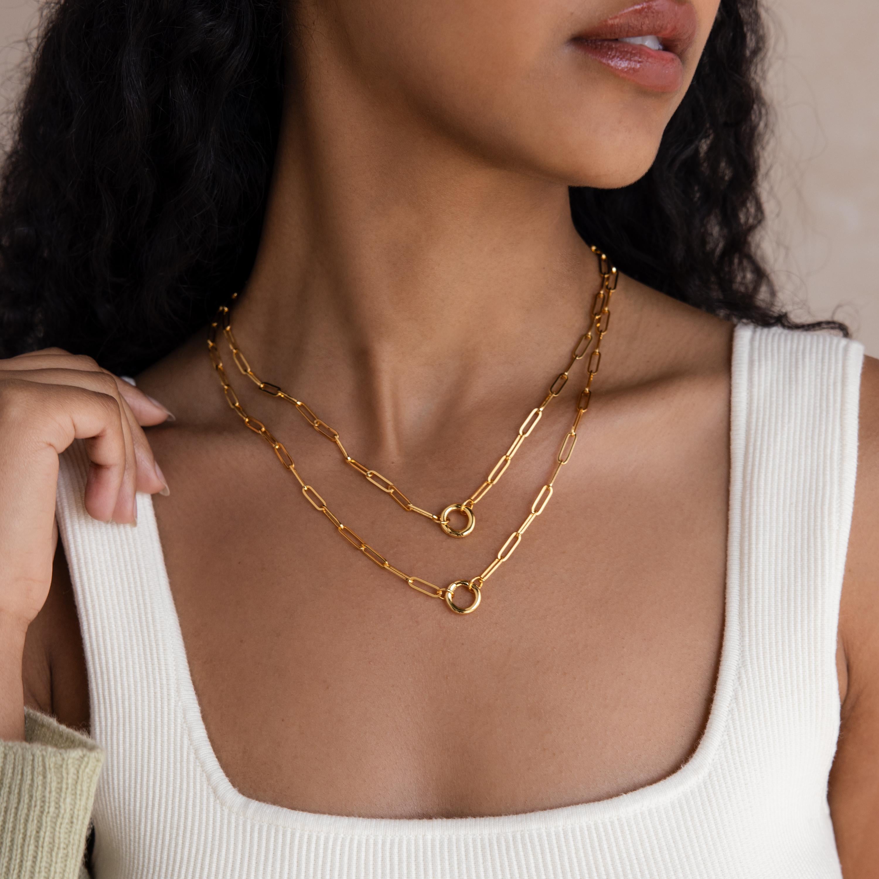 Woman wearing two gold chain necklaces, including the Paperclip Clasp Necklace with bold links and rings, paired with a cream ribbed tank top, shown from shoulders up.