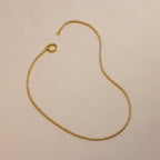The Diamond Tennis Clasp Necklace features small, evenly spaced diamonds and a secure rolo clasp, laid in an S-shape on a light beige background—a stunning choice for wedding jewelry.