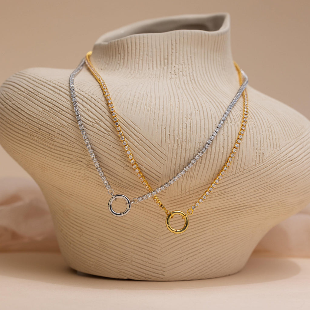 Two Diamond Tennis Clasp Necklaces—one in silver, one in gold—each with a round rolo clasp, displayed on a textured, neutral-toned bust. Timeless pieces perfect for wedding jewelry.