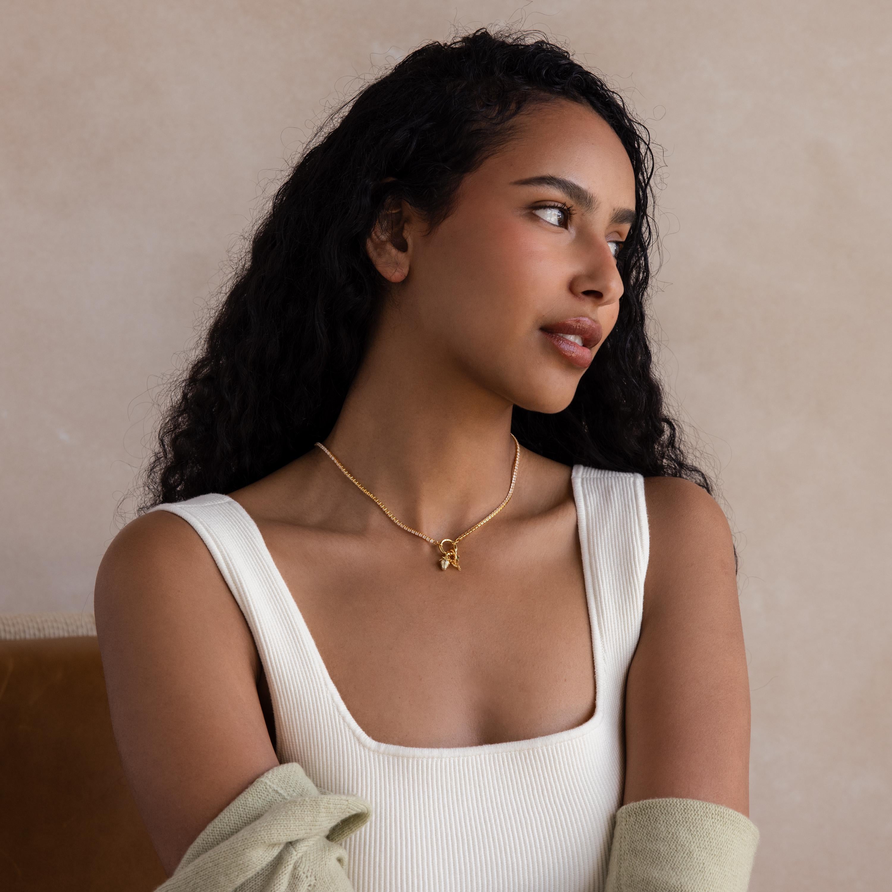 Woman with long curly hair wearing a white sleeveless top and the Diamond Tennis Clasp Necklace, featuring a rolo clasp, looking to the side against a neutral background.