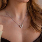 A woman wears the Rolo Heart Clasp Necklace, featuring a heart-shaped clasp, with a brown off-shoulder top.