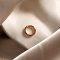 The Pave Ruby Charm Clip, featuring sparkling red stones, rests on silky beige and white fabric—ideal for jewelry personalization or as a distinctive charm holder.