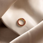 The Pave Ruby Charm Clip, featuring sparkling red stones, rests on silky beige and white fabric—ideal for jewelry personalization or as a distinctive charm holder.