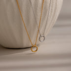 The Cable Circle Charm Necklace, available in gold and silver with a simple circular pendant, is displayed on a white vase. Wear it solo for a subtle statement or layer it for a minimalist look.