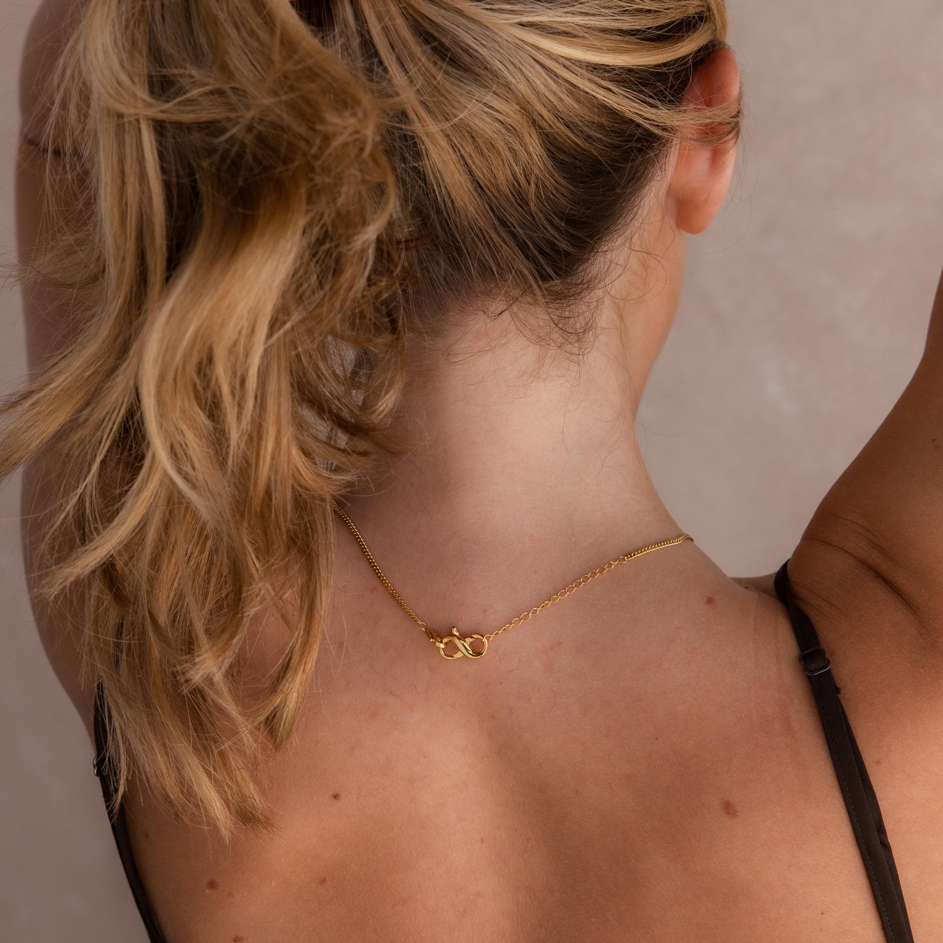 A woman with blonde hair in a ponytail displays the clasp of her gold necklace, lengthened and versatile thanks to the Multipurpose Lobster Clasp Extender Set in 18K Gold.