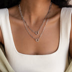A woman in a white ribbed square-neck top wears layered silver chain necklaces with circular pendants, featuring a bold link chain and the Paperclip Clasp Necklace.