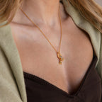 A woman wears the Multipurpose Charm Hoop Clasp Set in 18K Gold, styled with a letter A pendant and crystal charm, layered over a green cardigan and black top, creating a chic look with stacked bracelets.