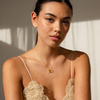A woman with straight dark hair wears the Pave Garnet Charm Clip on a gold necklace and a beige floral top, seated in soft natural light.