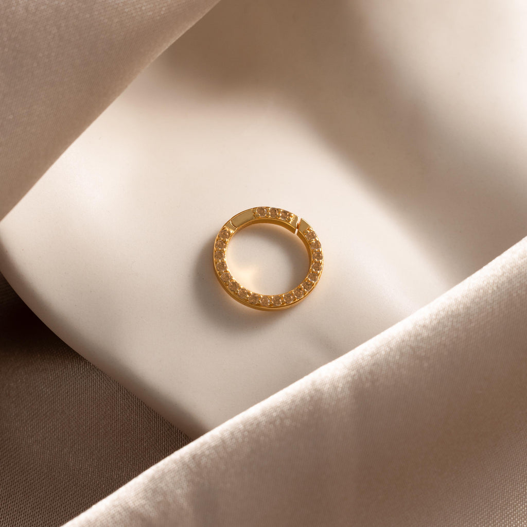 The Pave Topaz Charm Clip, adorned with sparkling gems and displayed on soft cream fabric, is the perfect accent for your personalized jewelry or charm holder.