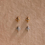 One pair of gold Pave North Star Earrings and one pair of silver Pave North Star Earrings displayed on a tan surface