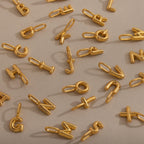 Bubble Letter Charms scattered on a beige surface—perfect for creating your own personalized jewelry collection.