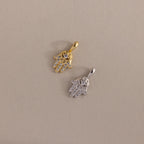 Two Pave Hamsa Hand Charms—one gold, one silver—adorned with clear stones, rest on a beige surface. These charms are perfect protection jewelry for anyone seeking spiritual clarity.