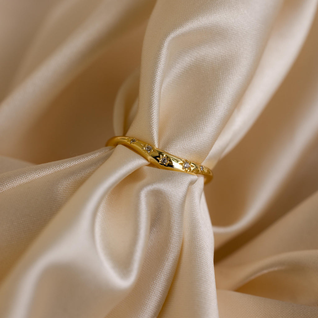 Close up of a gold celestial wave ring laying on a cloth surface