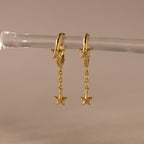 Close of Gold Star Drop Chain Huggie Earrings hanging from a glass.