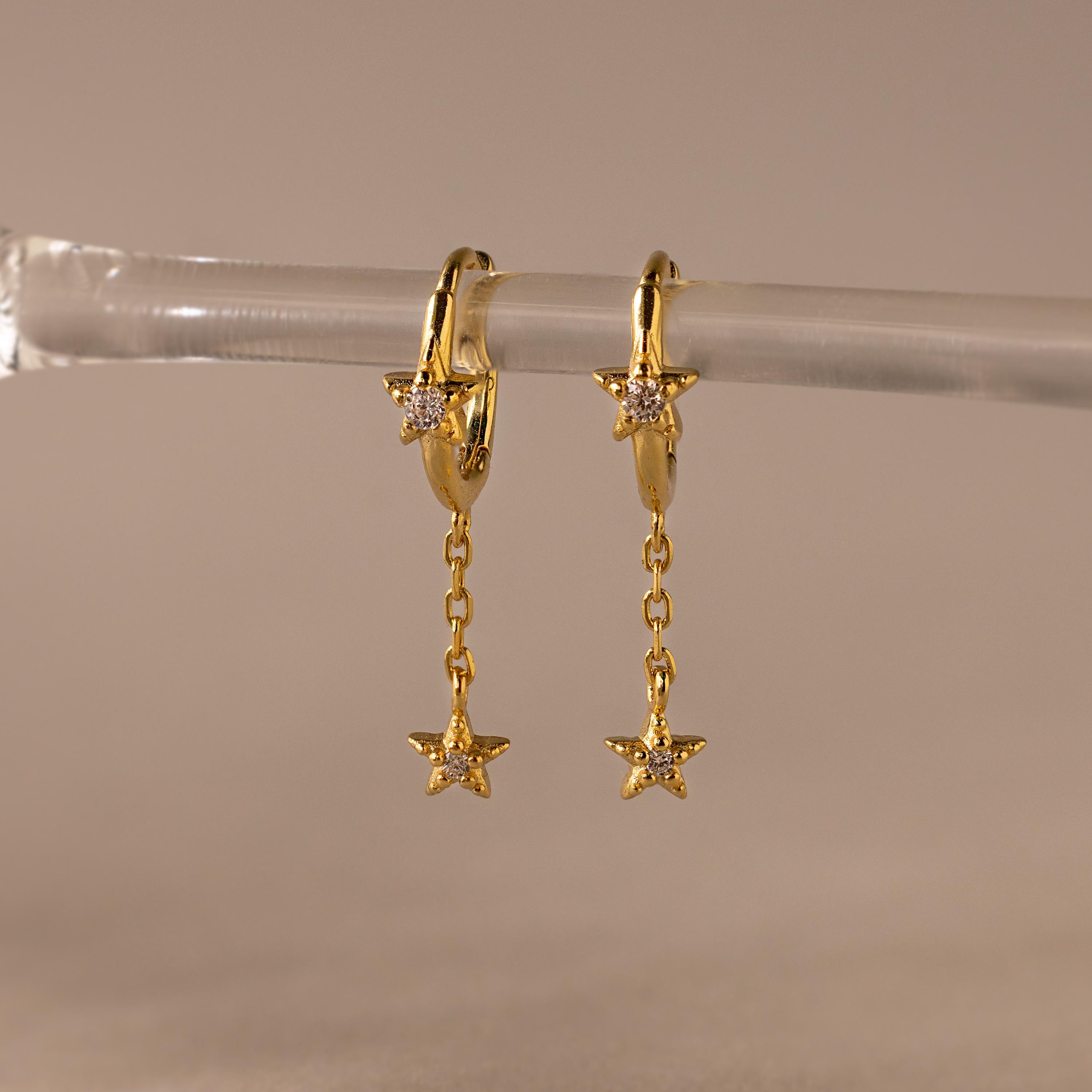 Close of Gold Star Drop Chain Huggie Earrings hanging from a glass.