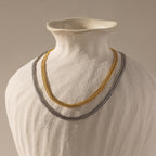 Flat lay of two Thick Mesh Chain Necklaces displayed on a sculptural ceramic bust—one in gold and the other in silver