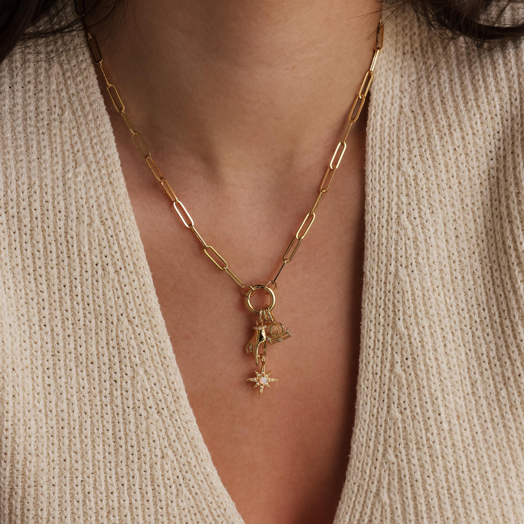 A close up of a rolo clasp charm necklace featuring the North Star Hand Charm and multiple other golden pendants