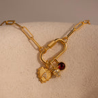A gold Ribbed Heart Initial Pendant with a pavé letter is styled on a carabiner clasp link necklace alongside a strawberry charm and a red garnet gemstone charm