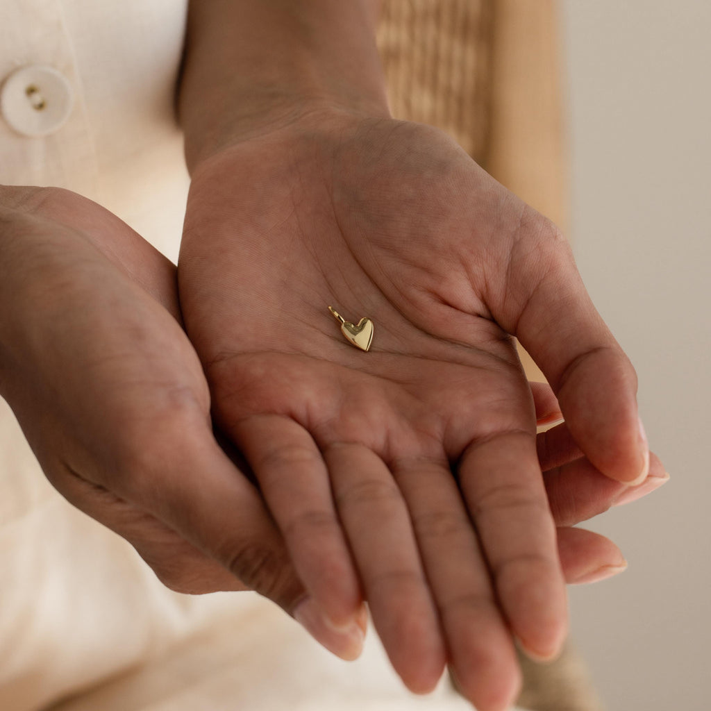 A close-up view of a hand cradling a single gold Simple Heart Charm, highlighting its compact size and glossy surface.