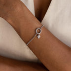 A silver bracelet with the silver Evil Eye Hand Charm attached to a circular clasp, styled on a model’s wrist.