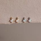 Two pairs of earrings — gold and silver — laid flat on textured beige paper.